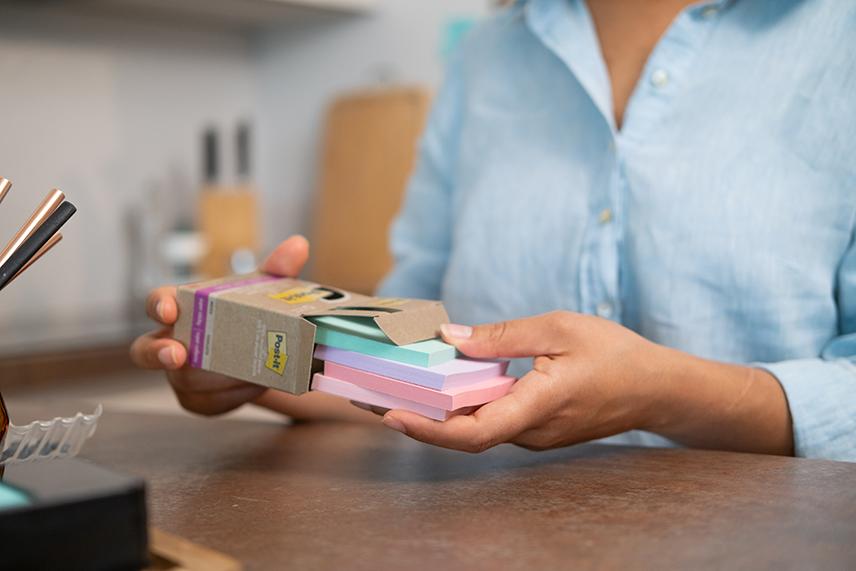 Woman shown holding a box of 3M Post-It sticky notes.